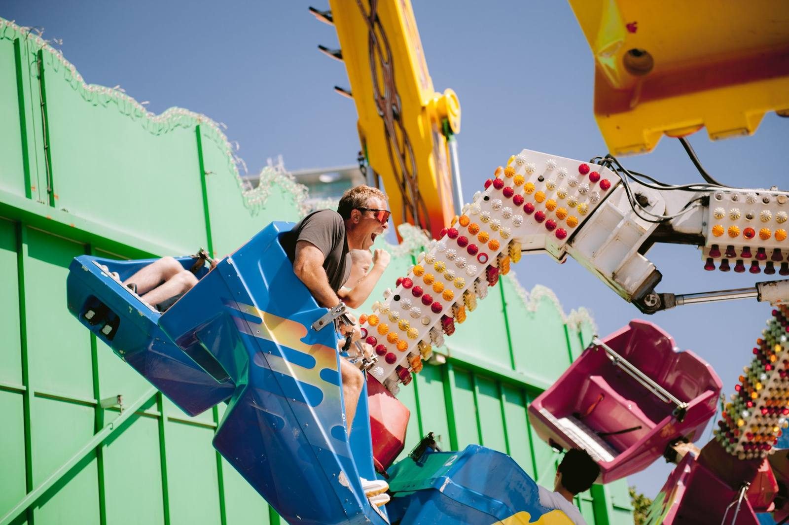 A vibrant scene of adults enjoying a thrilling amusement park ride under clear blue skies.