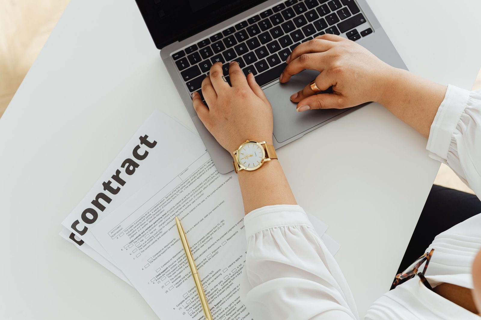 A woman using a laptop alongside a contract document on a desk, emphasizing business and legal themes.